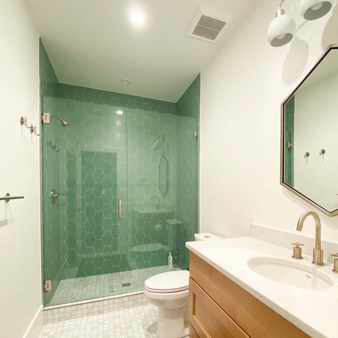 Spacious shower with green hexagonal tiles in a modern bathroom with wooden vanity.